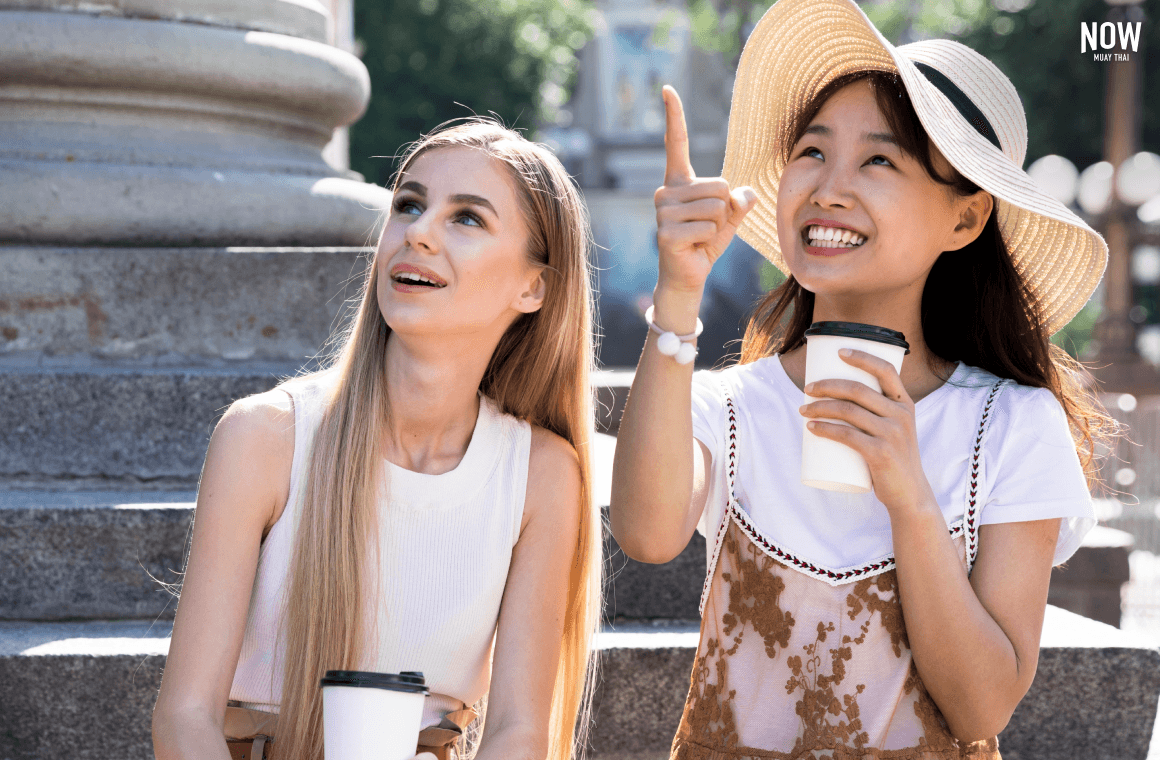 2 girls sitting on a stairs ouside, drinking coffee and talking